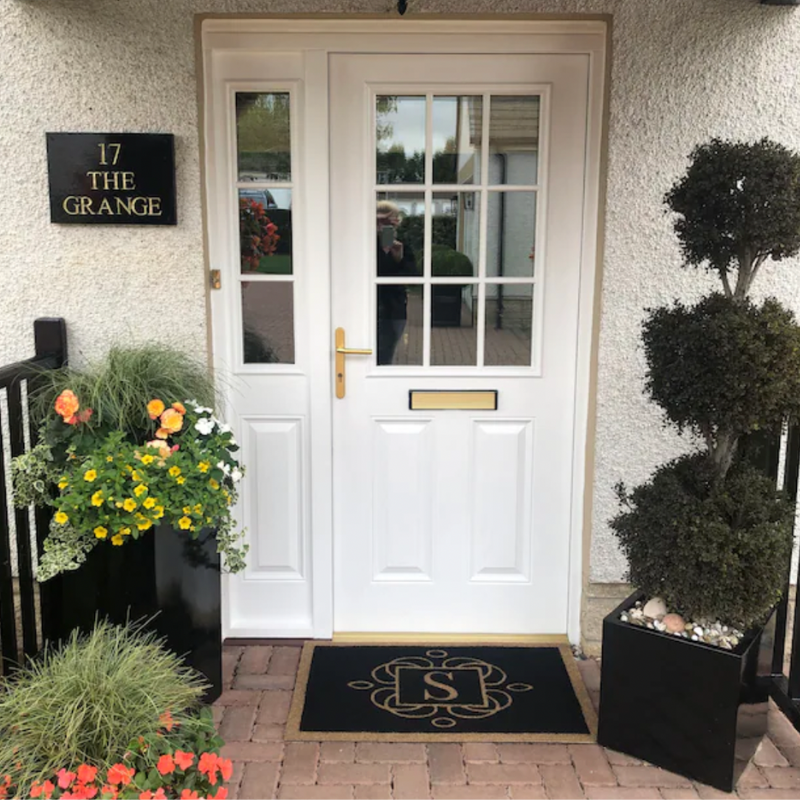 Black doormat with letter S and white door.